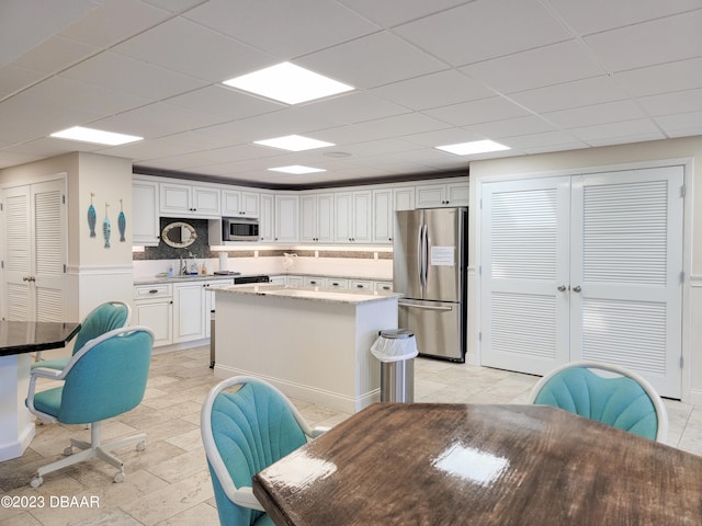 kitchen with appliances with stainless steel finishes, a drop ceiling, a kitchen island, white cabinets, and decorative backsplash