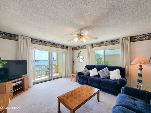 living room featuring ceiling fan, a water view, a textured ceiling, and a healthy amount of sunlight