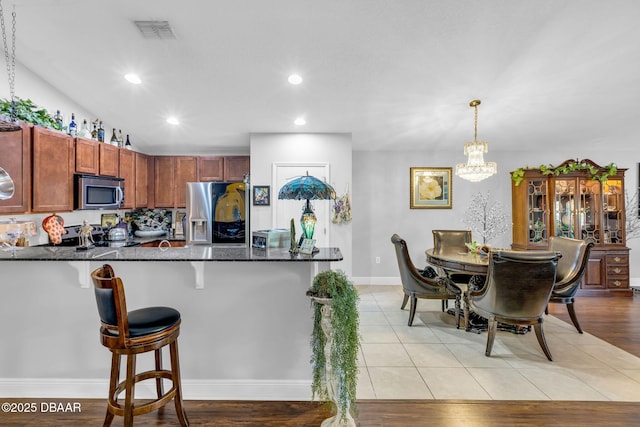 19343 Moorgate St, Orlando, FL 32833 - kitchen with appliances with stainless steel finishes, a peninsula, a breakfast bar area, dark stone countertops, and a chandelier
