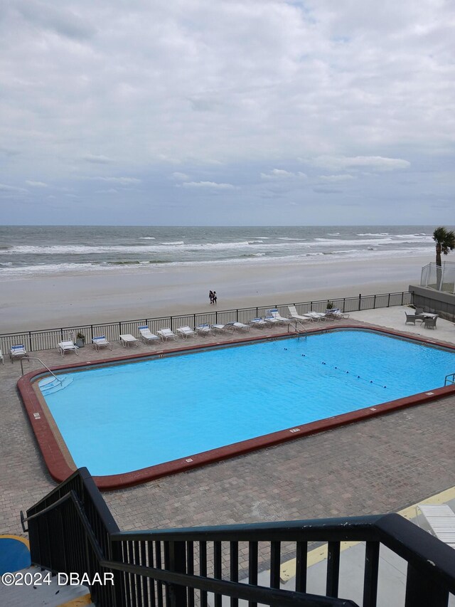 view of pool featuring a patio area, a water view, and a beach view