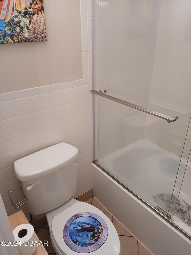 bathroom featuring tile walls, enclosed tub / shower combo, and toilet