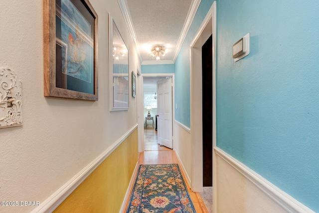 corridor with light wood-style flooring, crown molding, and a textured wall