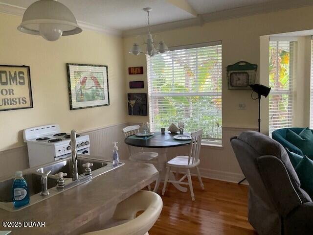 dining area with a wainscoted wall, a notable chandelier, crown molding, and wood finished floors