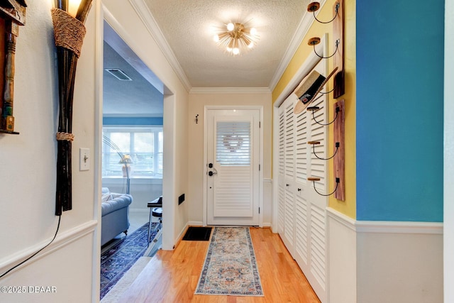 doorway to outside featuring visible vents, ornamental molding, a textured ceiling, light wood-type flooring, and baseboards