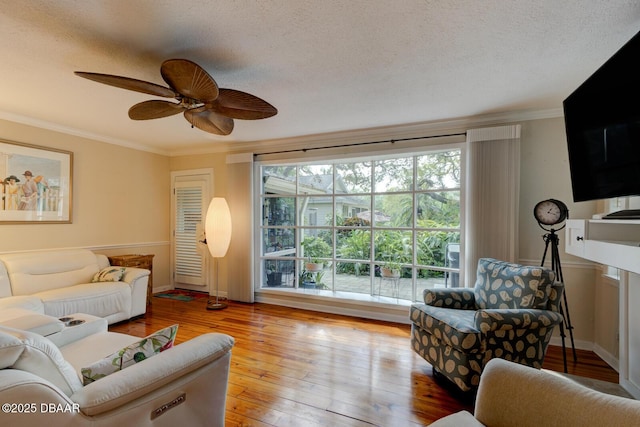 living area with ornamental molding, light wood-style floors, a ceiling fan, a textured ceiling, and baseboards