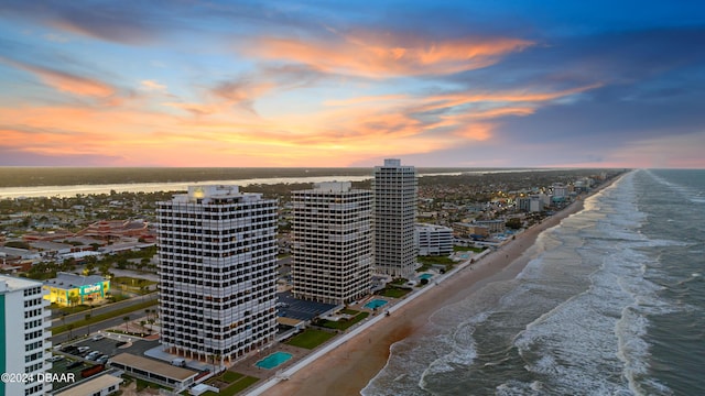 aerial view at dusk with a water view and a view of the beach