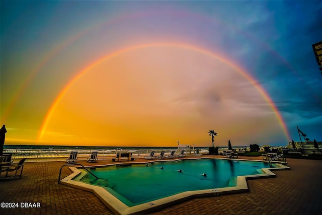 pool at dusk featuring a water view and a patio