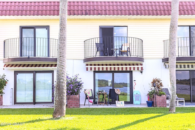 rear view of house with a lawn, a balcony, and a patio