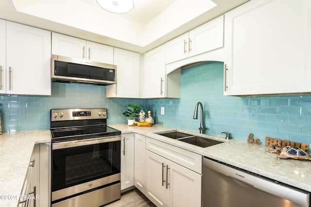 kitchen featuring light stone counters, white cabinets, sink, backsplash, and appliances with stainless steel finishes