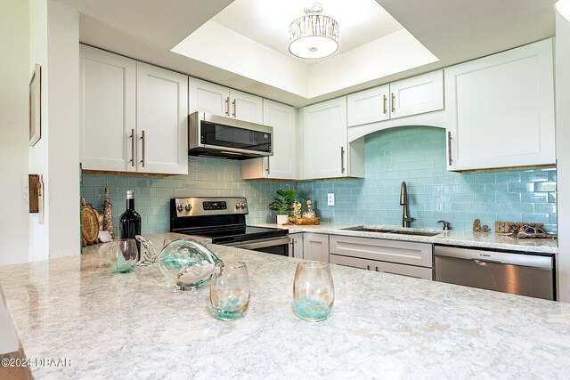 kitchen with white cabinets, appliances with stainless steel finishes, sink, and a tray ceiling