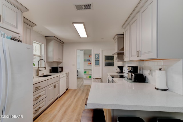 kitchen with white appliances, sink, light wood-type flooring, kitchen peninsula, and a breakfast bar area