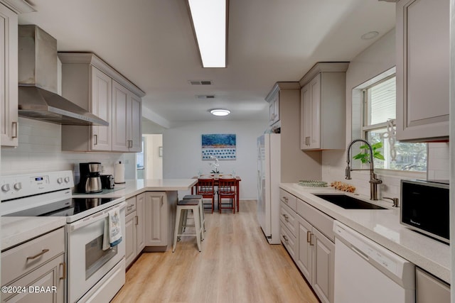 kitchen with wall chimney exhaust hood, a breakfast bar, white appliances, sink, and light hardwood / wood-style floors