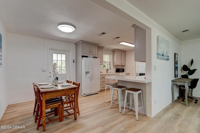 kitchen with gray cabinetry, a breakfast bar, light wood-type flooring, and white fridge with ice dispenser