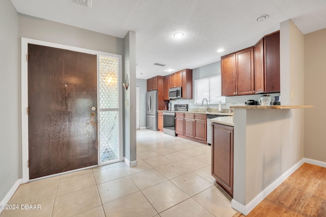 kitchen featuring appliances with stainless steel finishes, a textured ceiling, light stone counters, and light tile patterned floors