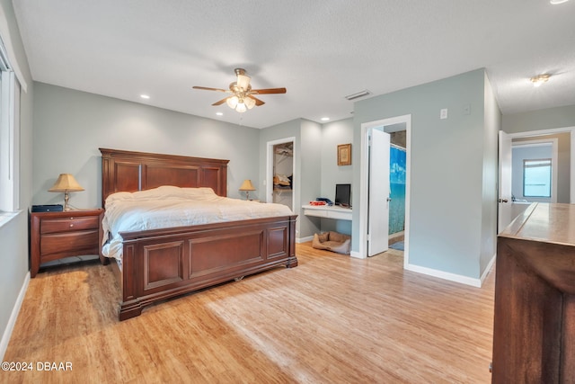 bedroom featuring light hardwood / wood-style floors, built in desk, ceiling fan, a spacious closet, and a closet