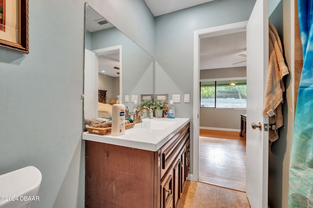 bathroom with toilet, vanity, wood-type flooring, and ceiling fan