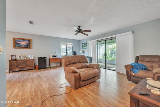 living room with ceiling fan, a textured ceiling, and light hardwood / wood-style flooring