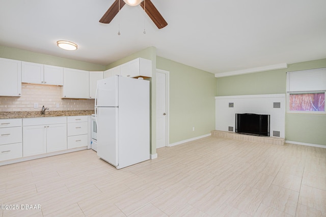 kitchen with freestanding refrigerator, white cabinets, a sink, and light stone countertops