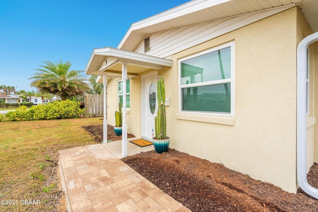 property entrance with a yard, fence, and stucco siding