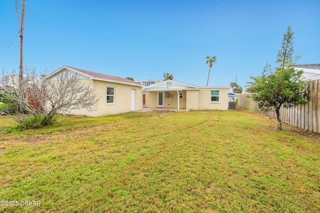 rear view of house featuring a yard, a fenced backyard, and stucco siding