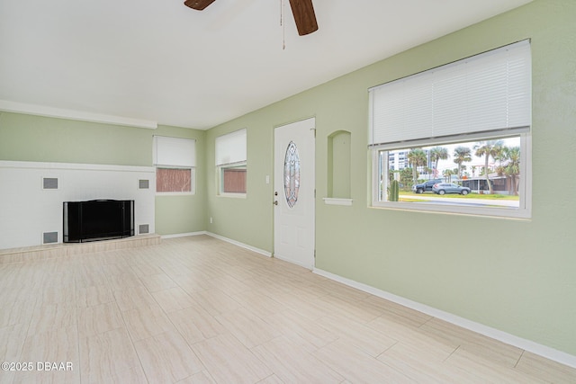 unfurnished living room featuring baseboards, visible vents, a fireplace with raised hearth, and a ceiling fan