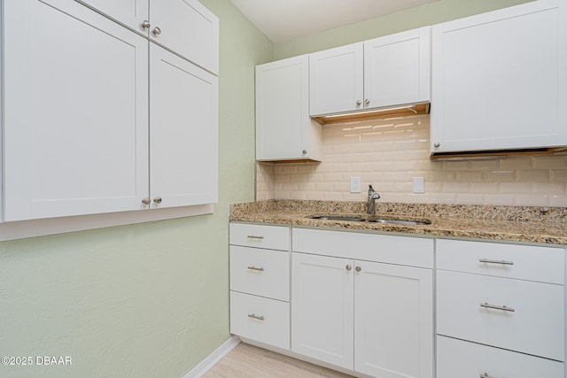 kitchen featuring tasteful backsplash, baseboards, light stone countertops, white cabinetry, and a sink