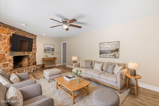 living room featuring ceiling fan, a fireplace, and light hardwood / wood-style floors