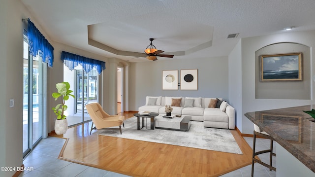 living room featuring a tray ceiling, ceiling fan, a textured ceiling, and light wood-type flooring