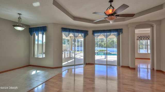 spare room featuring ceiling fan, light hardwood / wood-style floors, a textured ceiling, and a tray ceiling