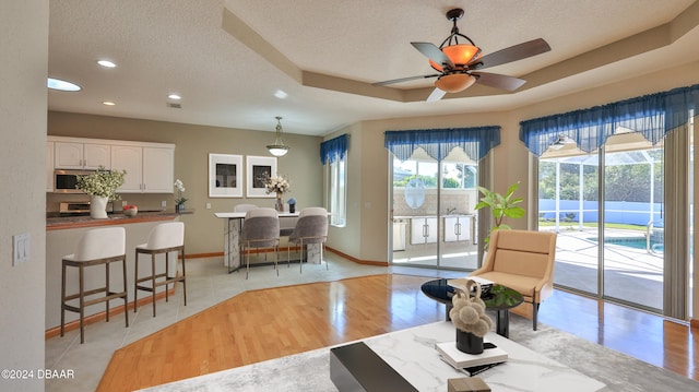 living room featuring ceiling fan, light wood-type flooring, a textured ceiling, and a tray ceiling