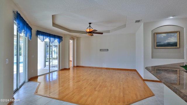 spare room featuring a textured ceiling, light wood-type flooring, a raised ceiling, and ceiling fan