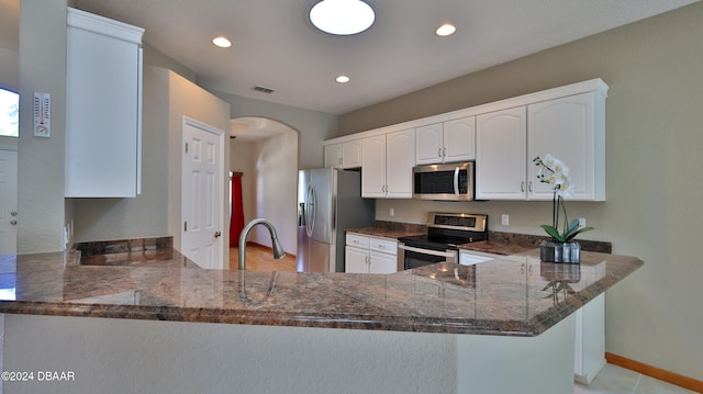 kitchen featuring white cabinetry, dark stone countertops, kitchen peninsula, and appliances with stainless steel finishes