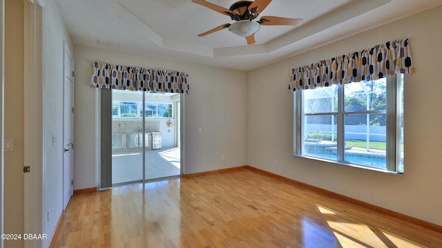 unfurnished room with a raised ceiling, light hardwood / wood-style flooring, and ceiling fan