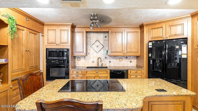 kitchen with tasteful backsplash, light stone counters, a breakfast bar, sink, and black appliances