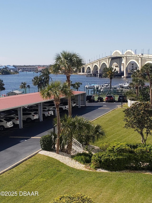 view of car parking with a lawn, a water view, and a carport