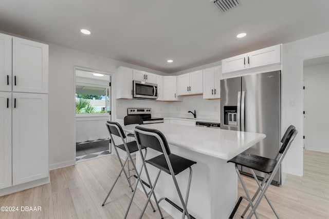 kitchen with white cabinets, a kitchen breakfast bar, light hardwood / wood-style flooring, appliances with stainless steel finishes, and a kitchen island