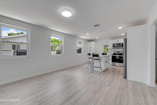 kitchen featuring a kitchen bar, appliances with stainless steel finishes, light wood-type flooring, white cabinets, and a kitchen island