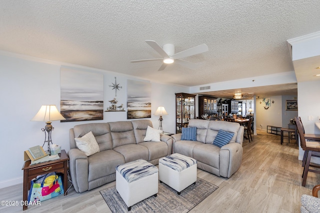 living area featuring a textured ceiling, ceiling fan, light wood finished floors, crown molding, and baseboards