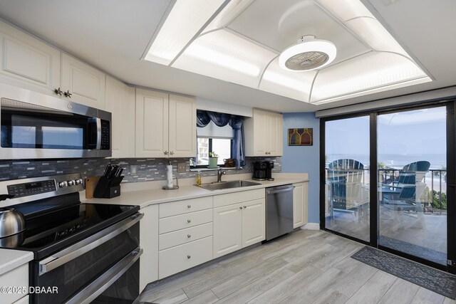 kitchen with stainless steel appliances, a sink, light wood finished floors, light countertops, and tasteful backsplash