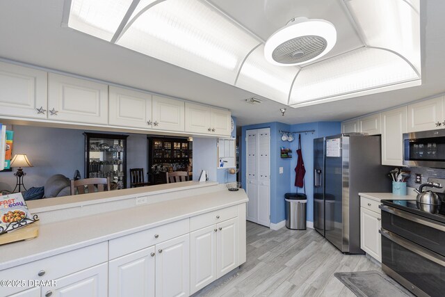 kitchen featuring stainless steel appliances, light countertops, white cabinets, light wood finished floors, and baseboards