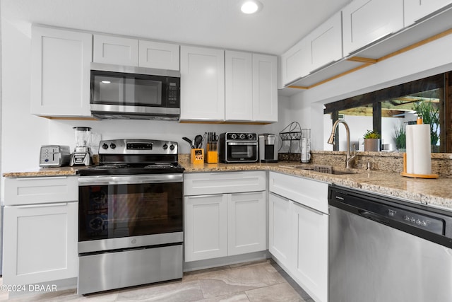 kitchen with white cabinets, sink, light stone countertops, and stainless steel appliances