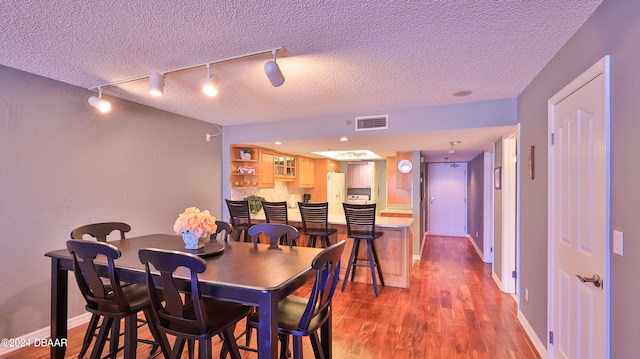 dining room featuring rail lighting, wood-type flooring, and a textured ceiling