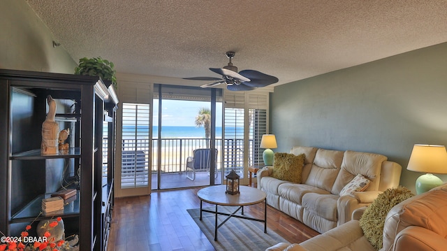 living room with dark hardwood / wood-style flooring, a water view, a textured ceiling, and ceiling fan