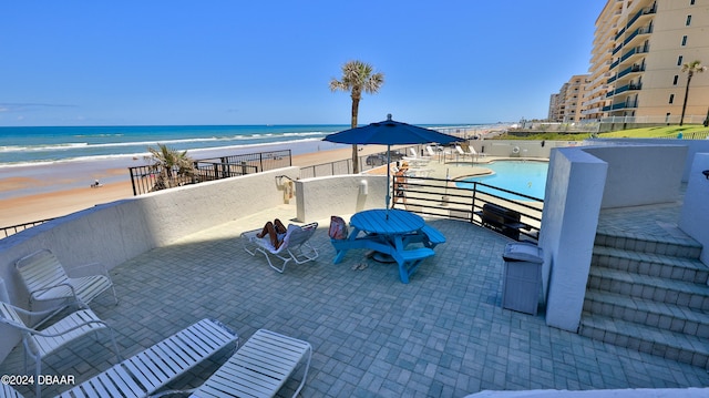 view of patio with a beach view, a water view, and a community pool