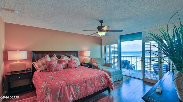 bedroom featuring access to outside, a textured ceiling, dark hardwood / wood-style flooring, a water view, and ceiling fan