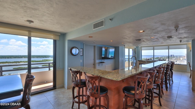 kitchen featuring light tile patterned flooring, plenty of natural light, a water view, and light stone counters