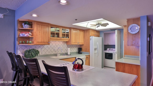 kitchen with white appliances, washer / clothes dryer, sink, kitchen peninsula, and ceiling fan