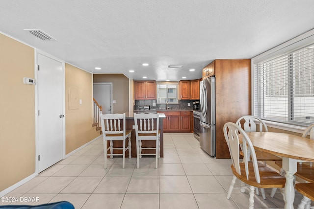 kitchen with a center island, a textured ceiling, a kitchen breakfast bar, backsplash, and appliances with stainless steel finishes