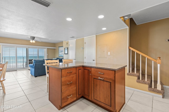 kitchen with a textured ceiling, stone counters, ceiling fan, and light tile patterned floors