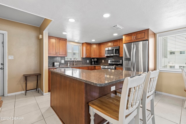 kitchen with stainless steel appliances, light tile patterned floors, decorative backsplash, a kitchen breakfast bar, and a center island